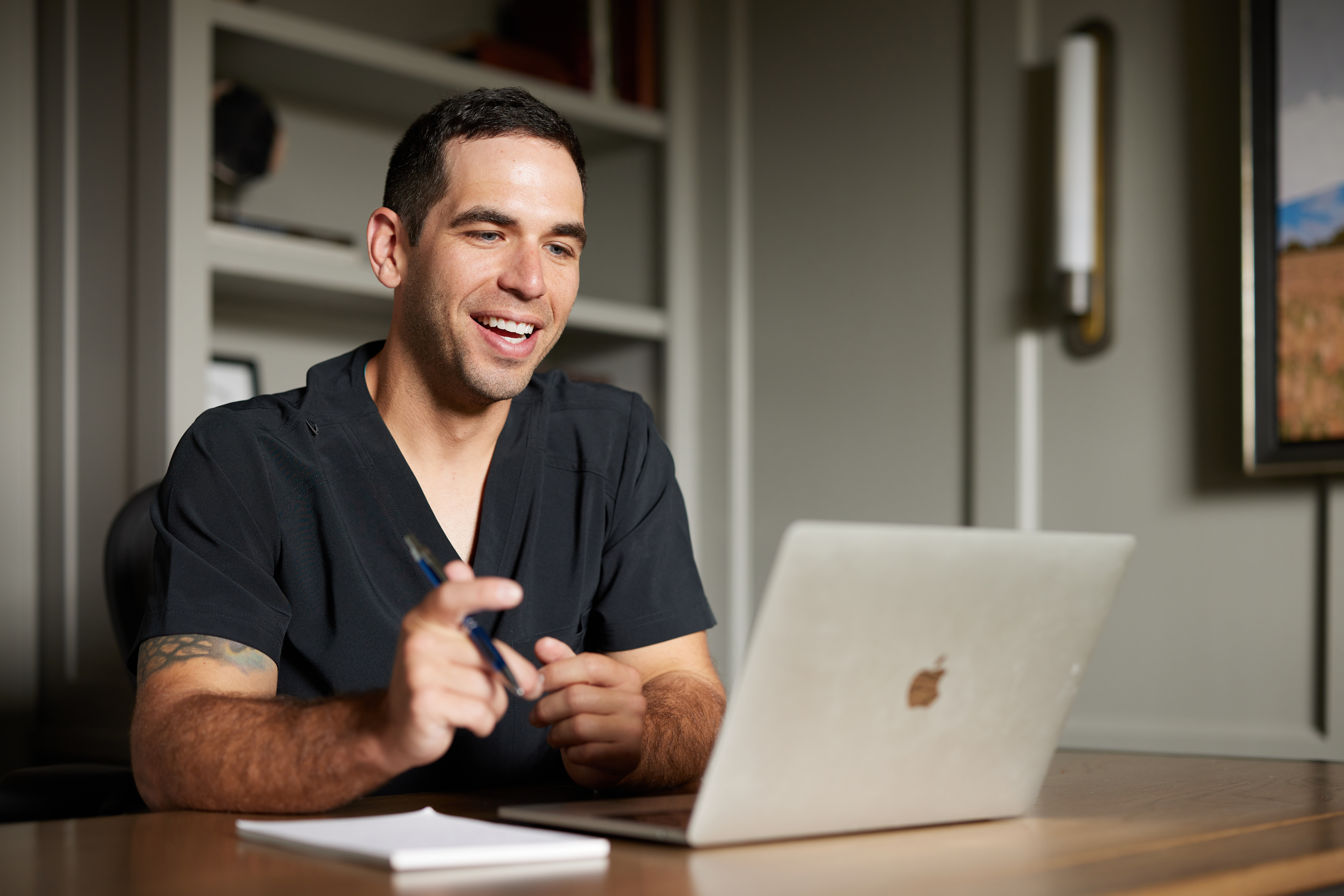 Dentist wearing dark scrubs reviewing finances on his computer in a home office